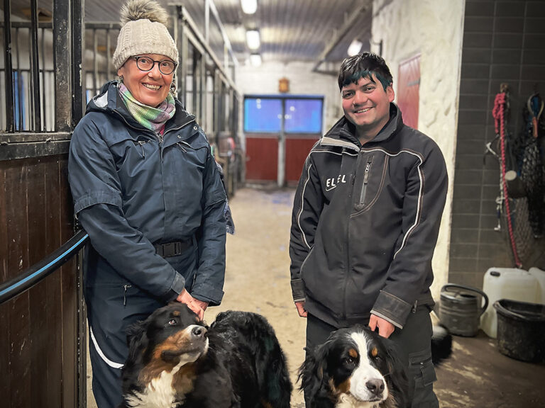 Maija och Jonas stål i stallgången på gården Lyckodalen tillsammans med sina två hundar.